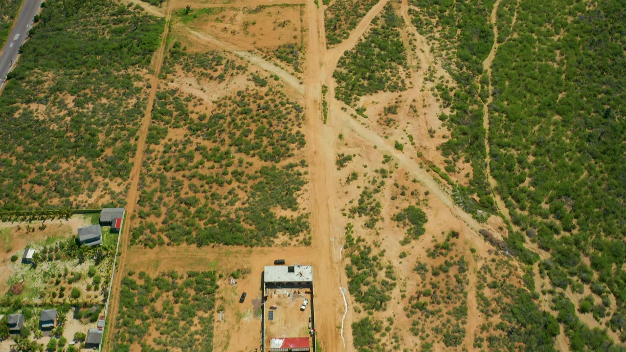 Aerial view of scrubland and dirt tracks with buildings and vehicles along the left edge.
