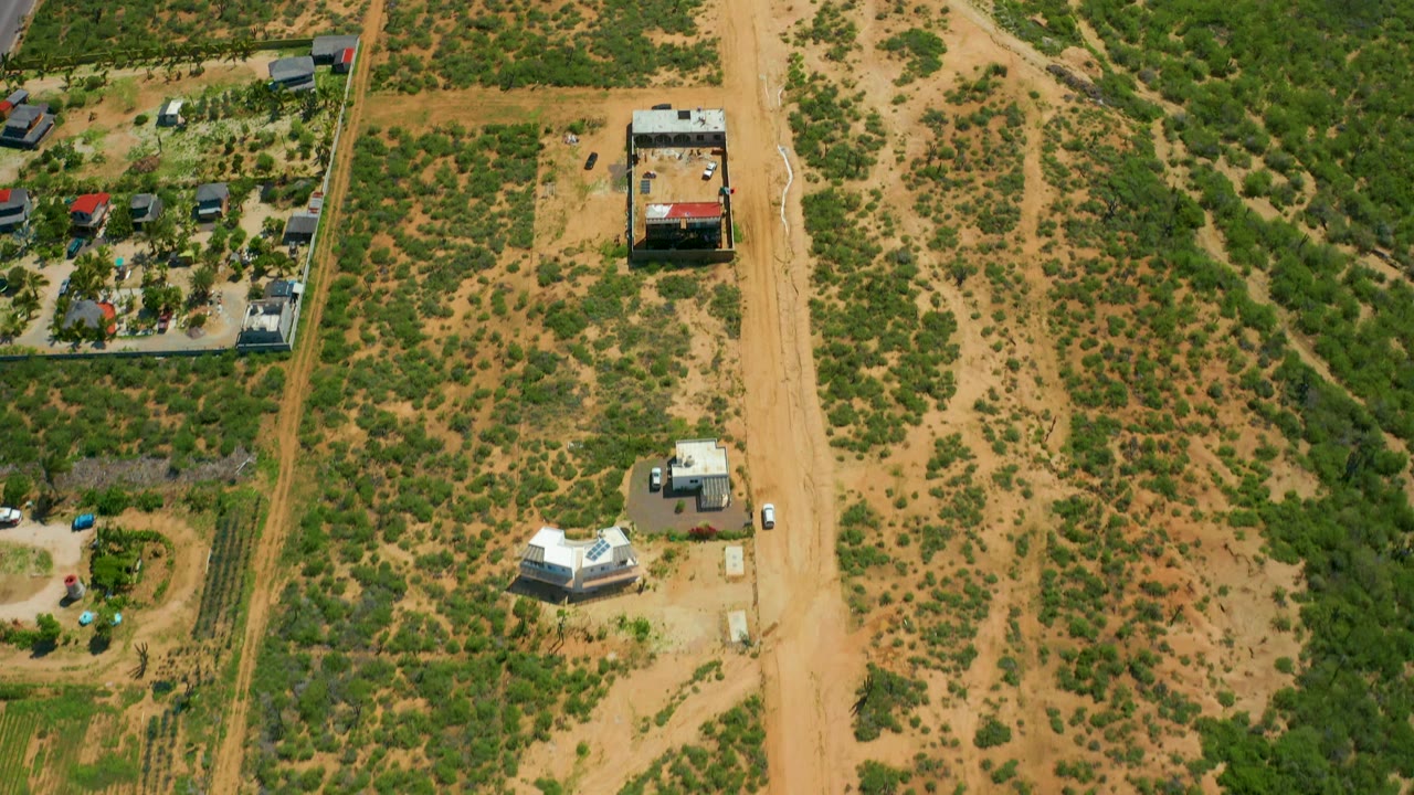 Aerial view of a sandy road beside desert vegetation, buildings, and a small parking area.