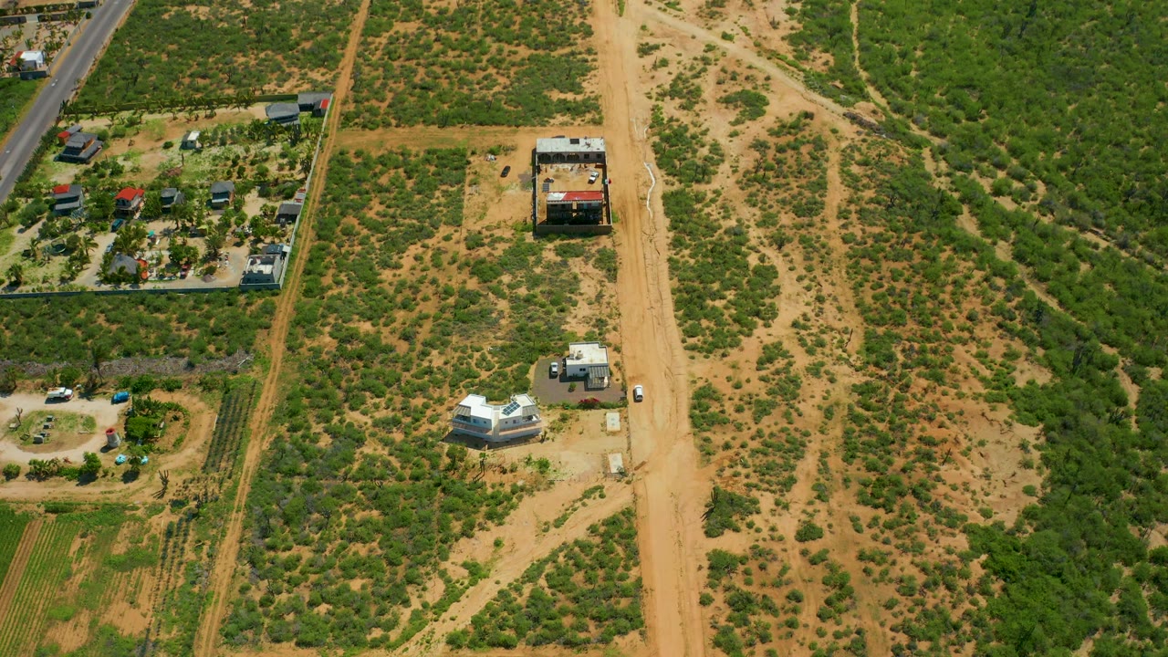 Overhead rural landscape with small structures, a dirt road, and scrubland.