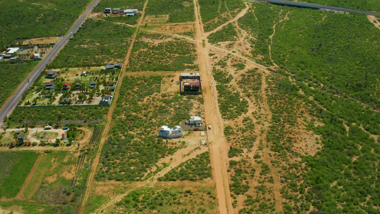 Aerial view of rural roads, cultivated patches, scrubland, buildings, and small vehicles.