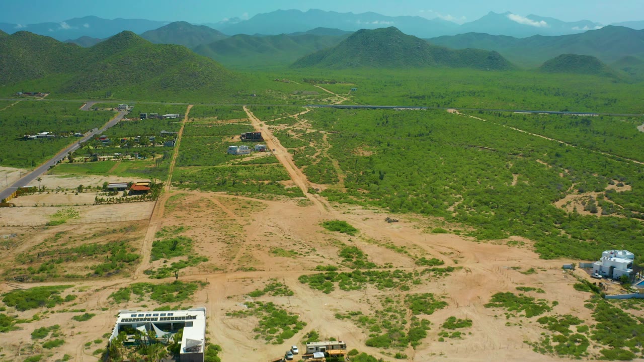 Drone view of a paved road, dirt road, small structures, and green mountain valley.