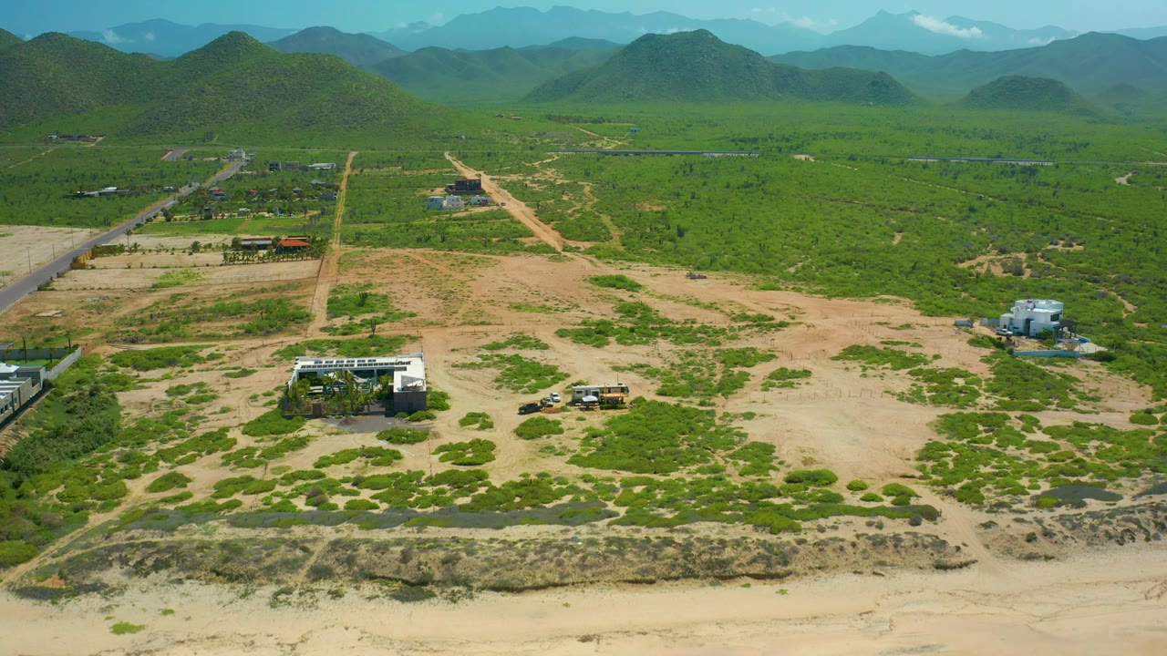Aerial landscape with sandy foreground, green scrub, road corridors, buildings, and hills.
