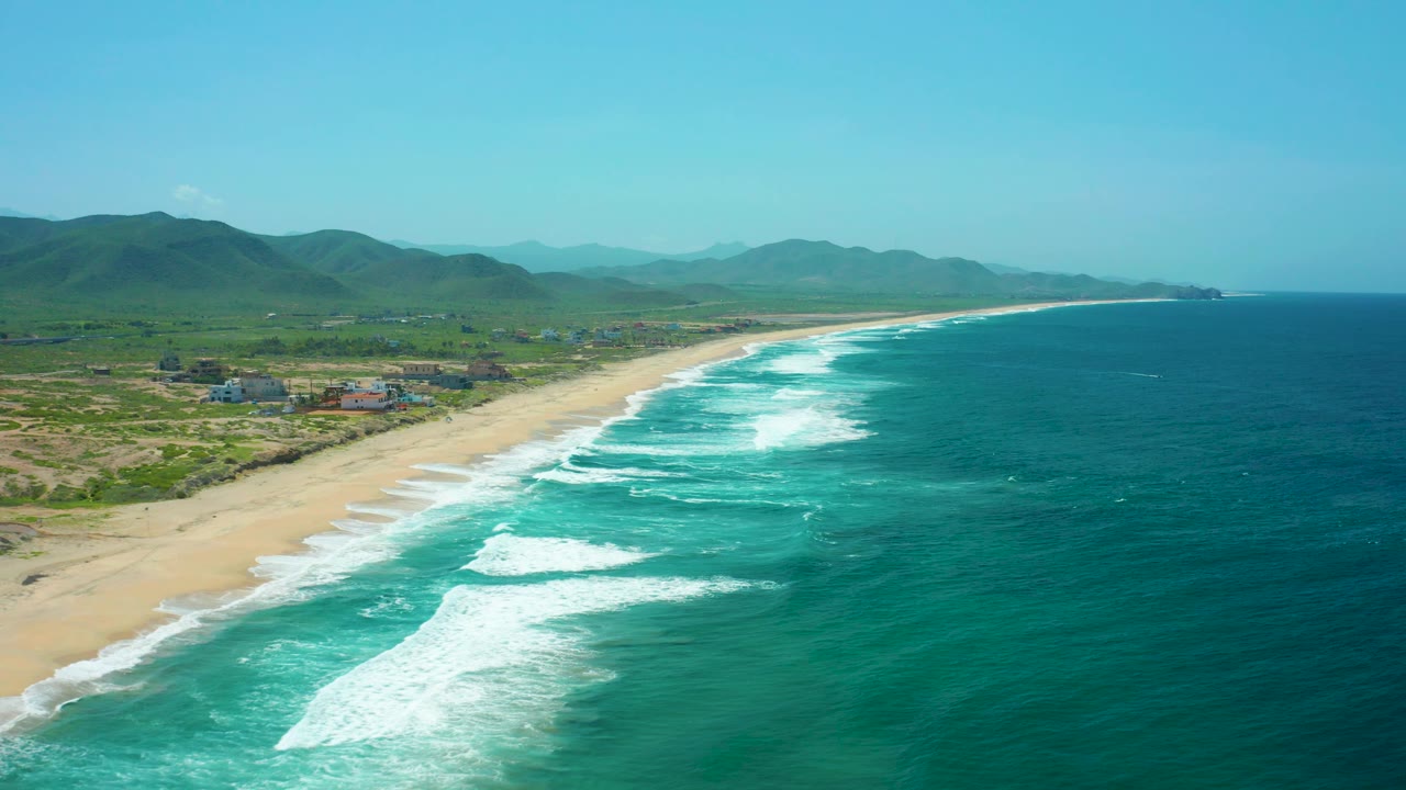 Drone view of surf breaking beside a wide sandy beach