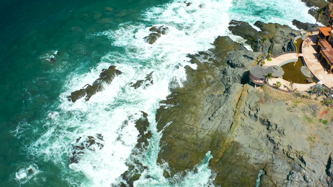 At 0:01 in Cerritos Beach, whitewater spreads across the central rocks while green ocean remains on the left and the coastal structure stays near the right edge, with no visible people.