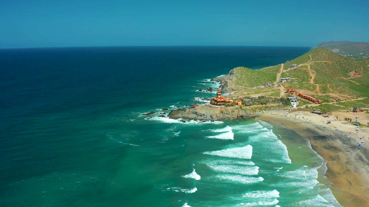 At 0:03, the aerial composition holds open water across the left half while waves break near the lower right sand, the coastal hill and dirt tracks remain in the background, and no visible people appear.