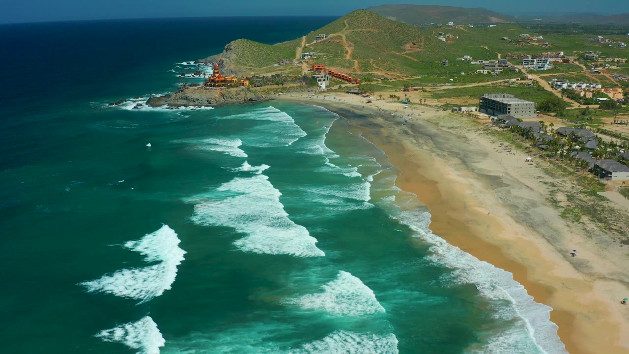 Drone view down a beach with breaking waves and a rocky point in the distance.
