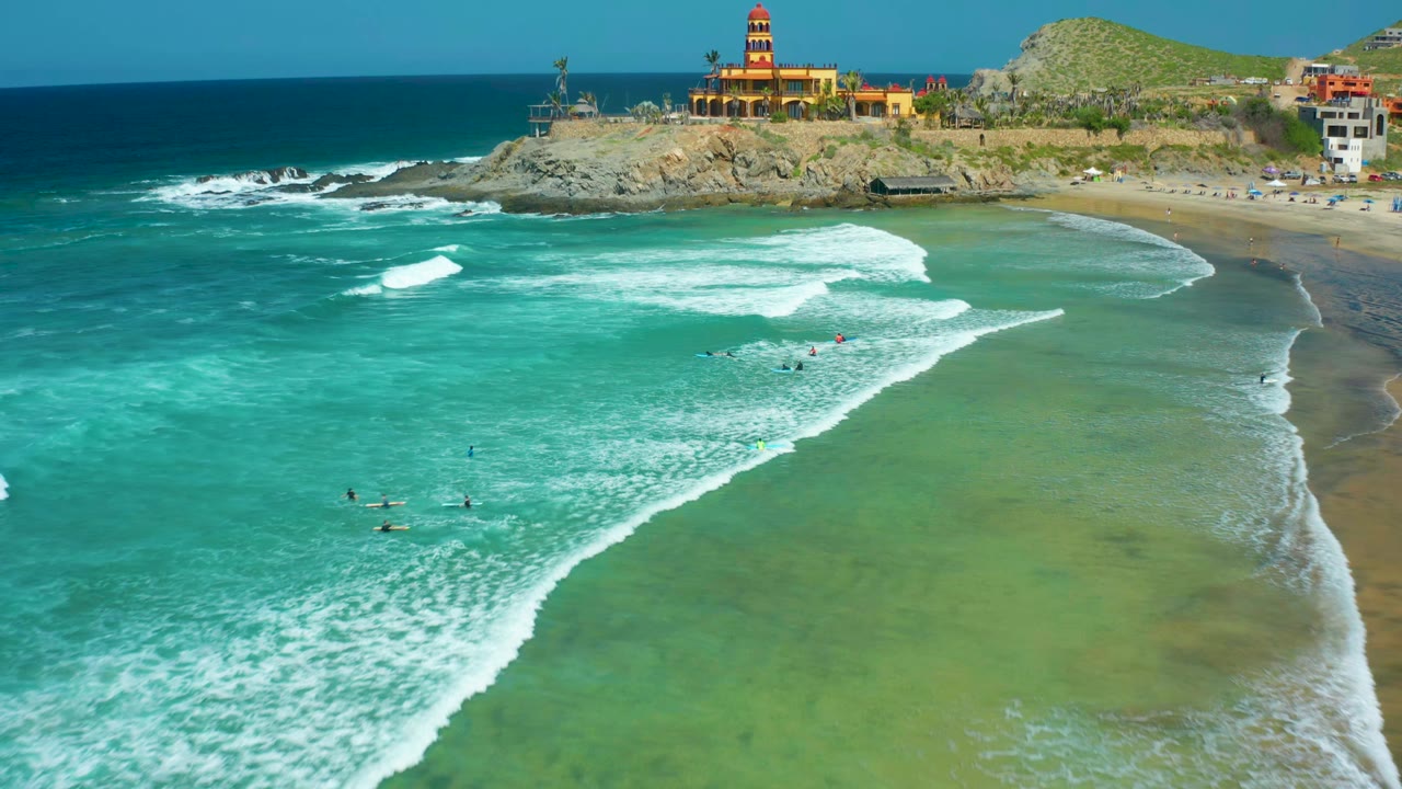 High aerial view of surfers and swimmers in turquoise water near shore.