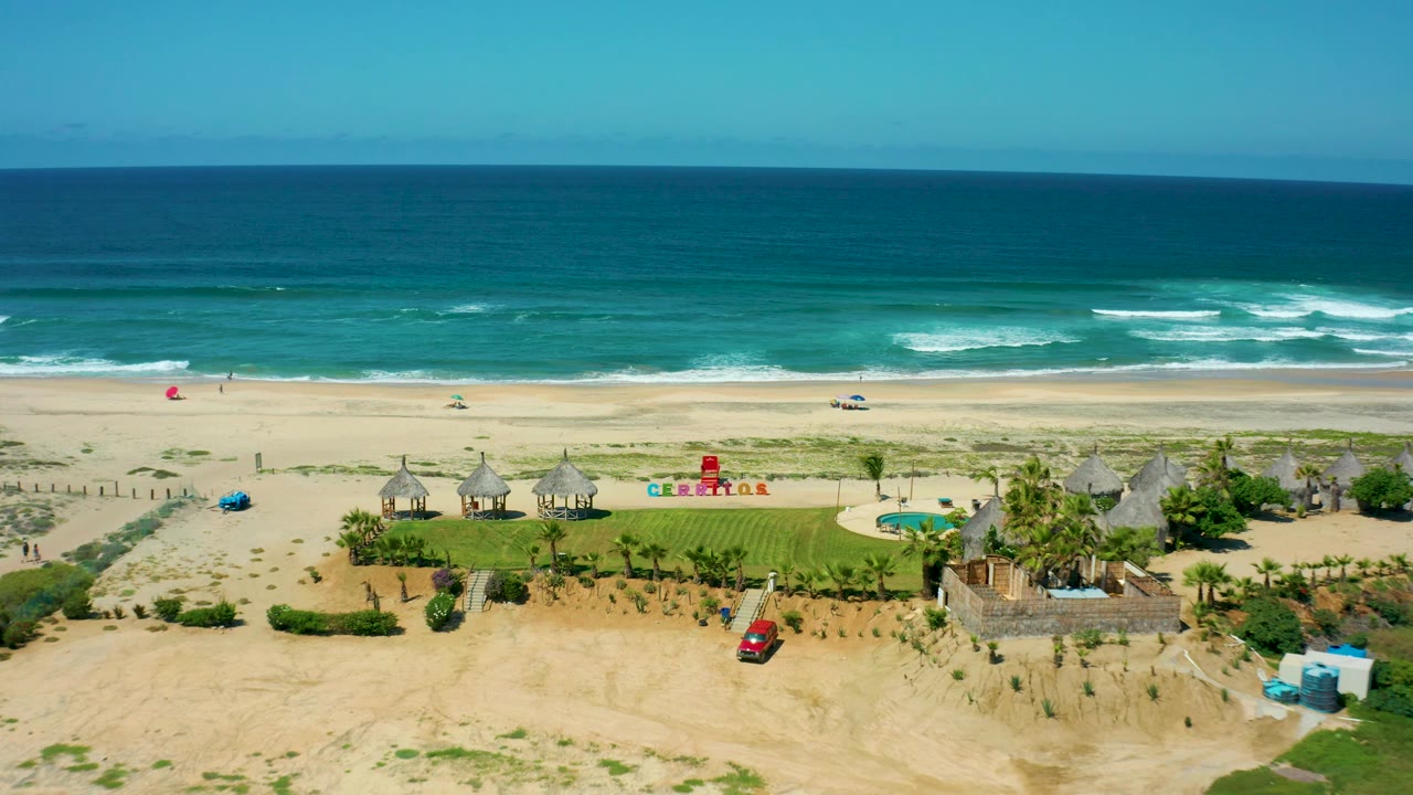 Drone view of Cerritos Beach surf behind resort huts and lawn.