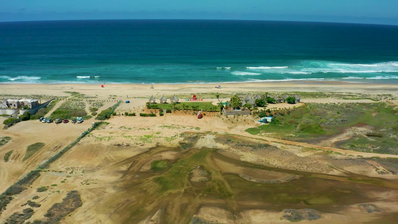 High beach view with waves, vehicles, dunes, and dirt tracks.
