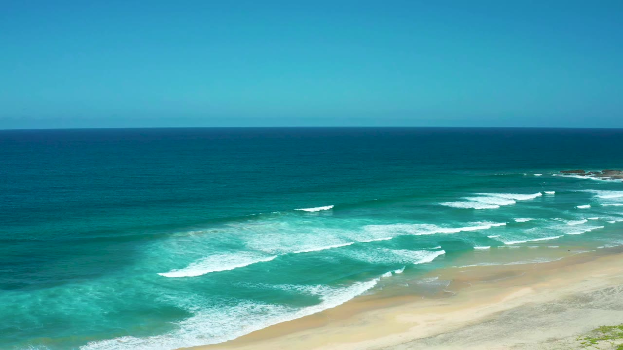 Cerritos Beach shoreline with diagonal white wave lines moving toward the sand, open blue water beyond, and no visible people in the frame.