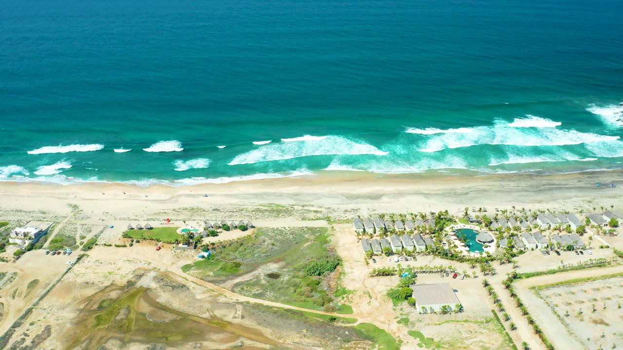 Aerial shoreline with breaking surf above a pool and beachfront structures