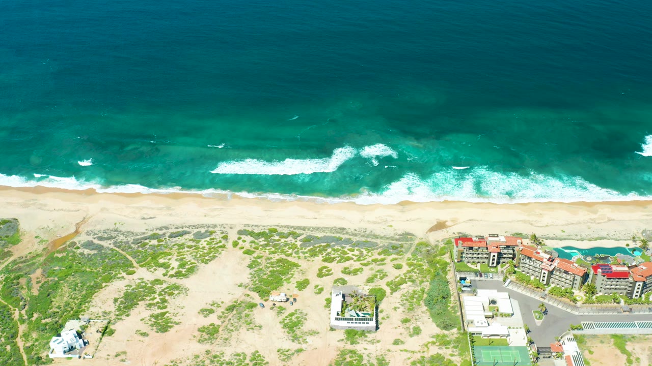 Overhead surf and sandy beach with dunes and buildings below