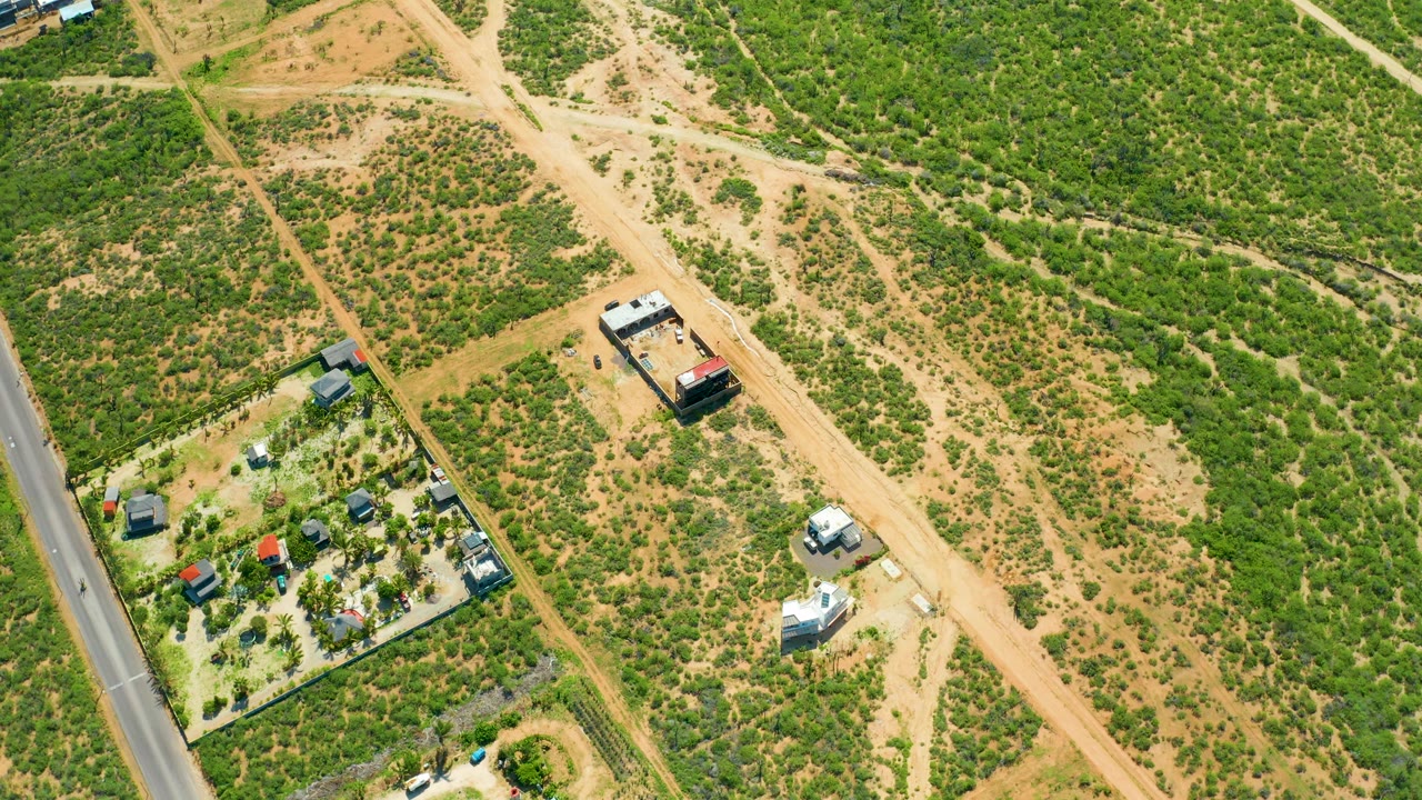 Overhead view of intersecting dirt roads, scrubland, and a white van near small buildings.