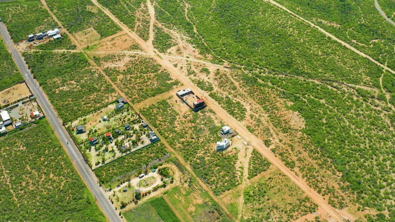 Drone view over Cerritos Beach, Baja California Sur, showing the paved roadside, branching dirt tracks, small buildings, parked vehicles, and no visible people.