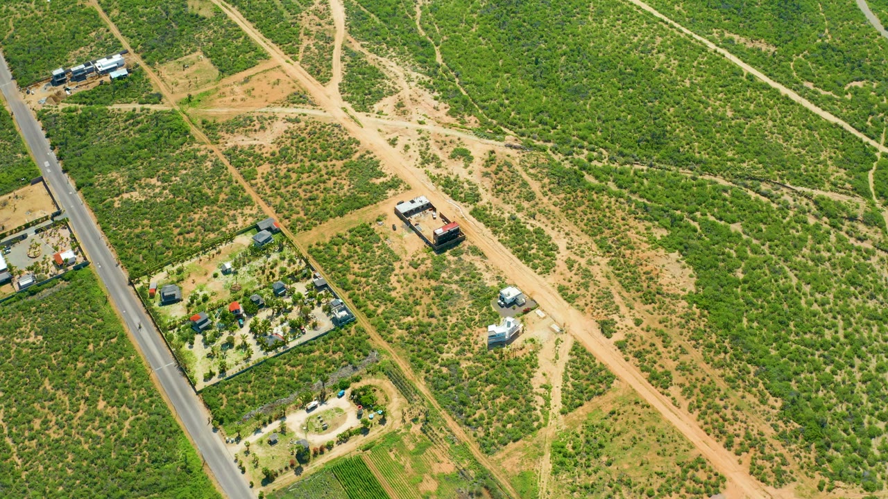 High aerial view of a rural paved road beside dirt paths and green open land.