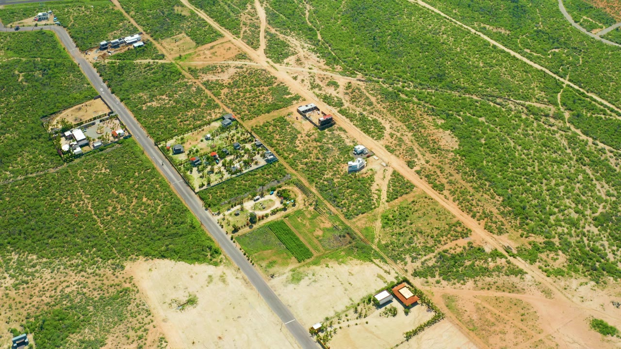 Opening aerial frame near Cerritos Beach, Mexico, showing a paved rural road crossing green scrub and tan dirt paths with small buildings and no visible people.