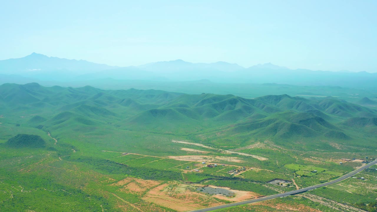 Wide aerial view of rural road, fields, and rolling green hills