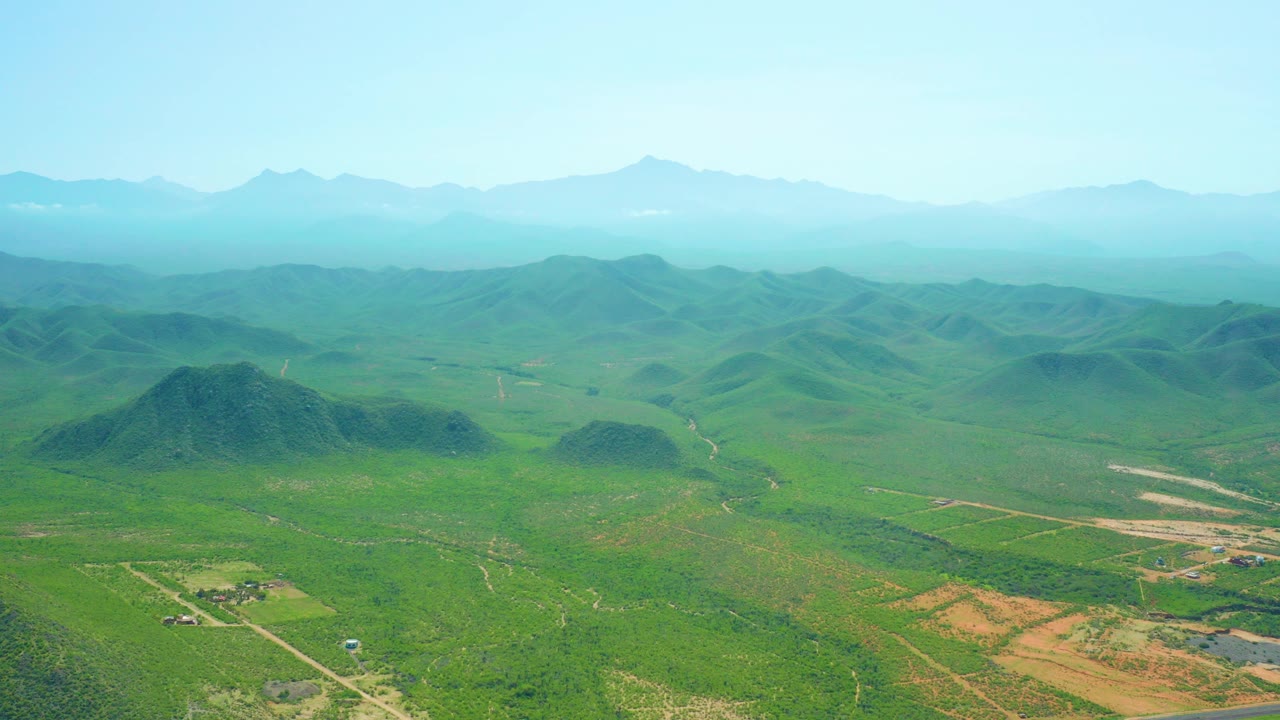 Opening frame of Cerritos Beach, Baja California Sur countryside with green hills, farmland grids, pale roads, hazy mountains, and no visible people.