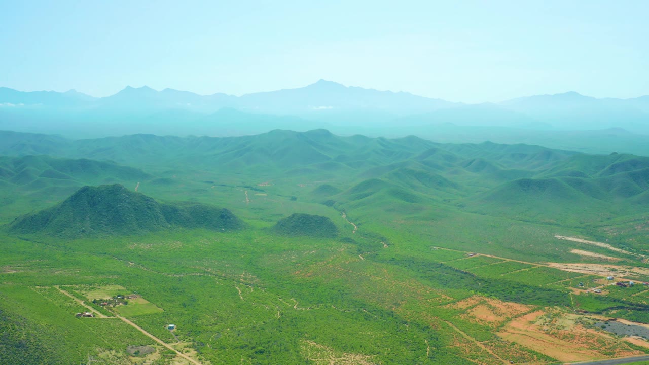 Third frame holds on green agricultural terrain near Cerritos Beach, with scattered hills, road lines crossing the fields, hazy mountains, and no visible people.