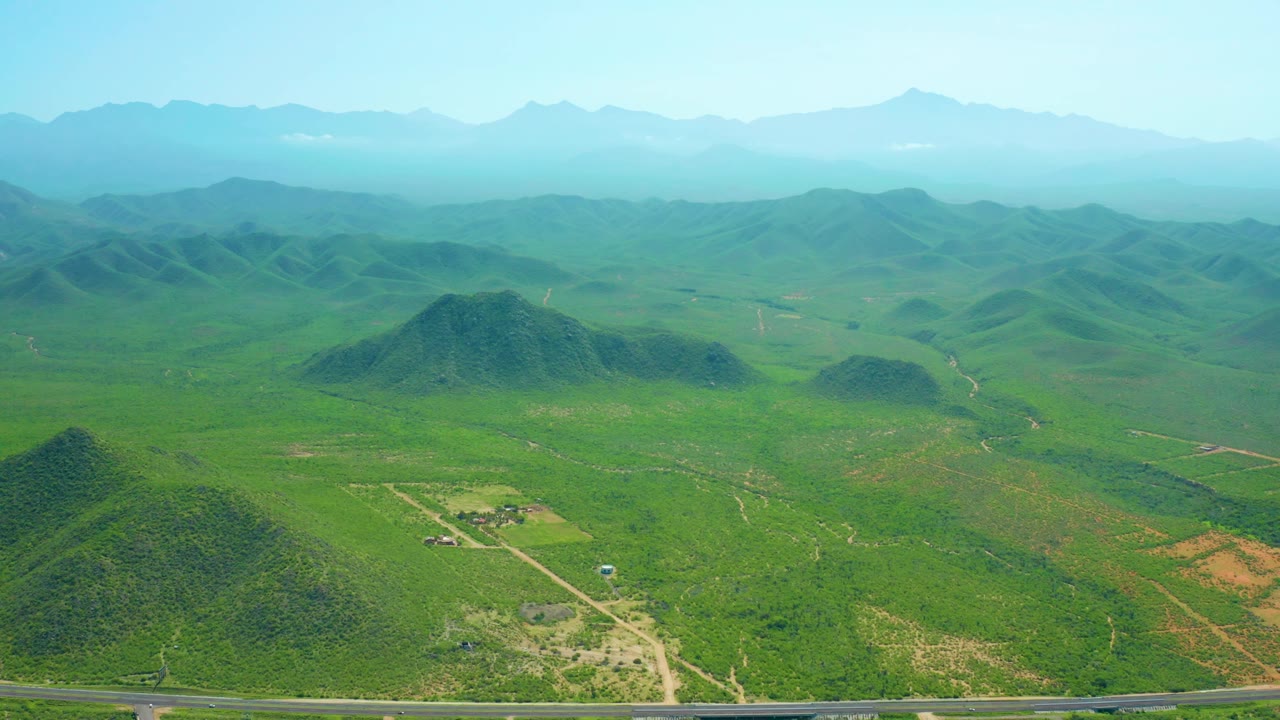 Wide aerial view of green hills with a road and hazy mountains.
