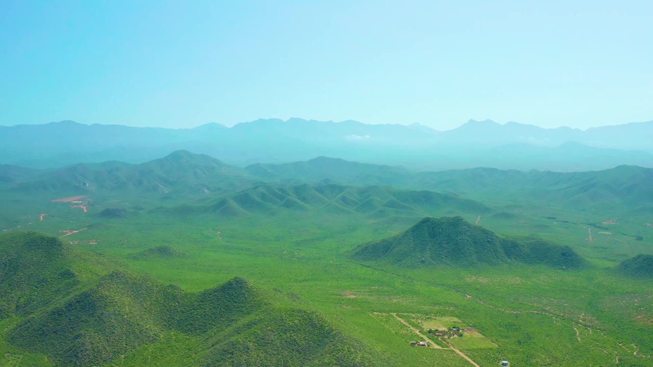 Green valley with rounded hills and distant mountain ridges.