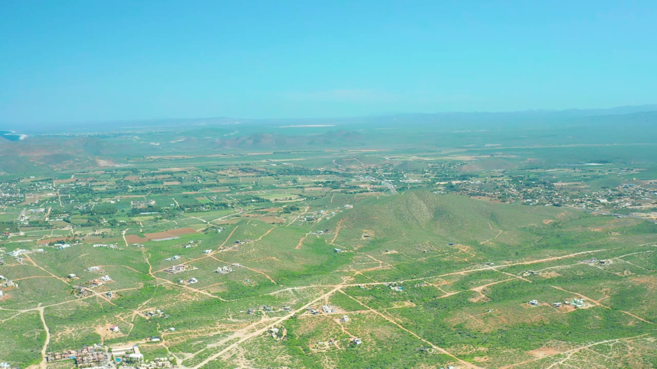 Cerritos Beach, Baja California Sur rural landscape seen from above, with more central dirt-road lines crossing green terrain, small building clusters in the distance, and no visible people.