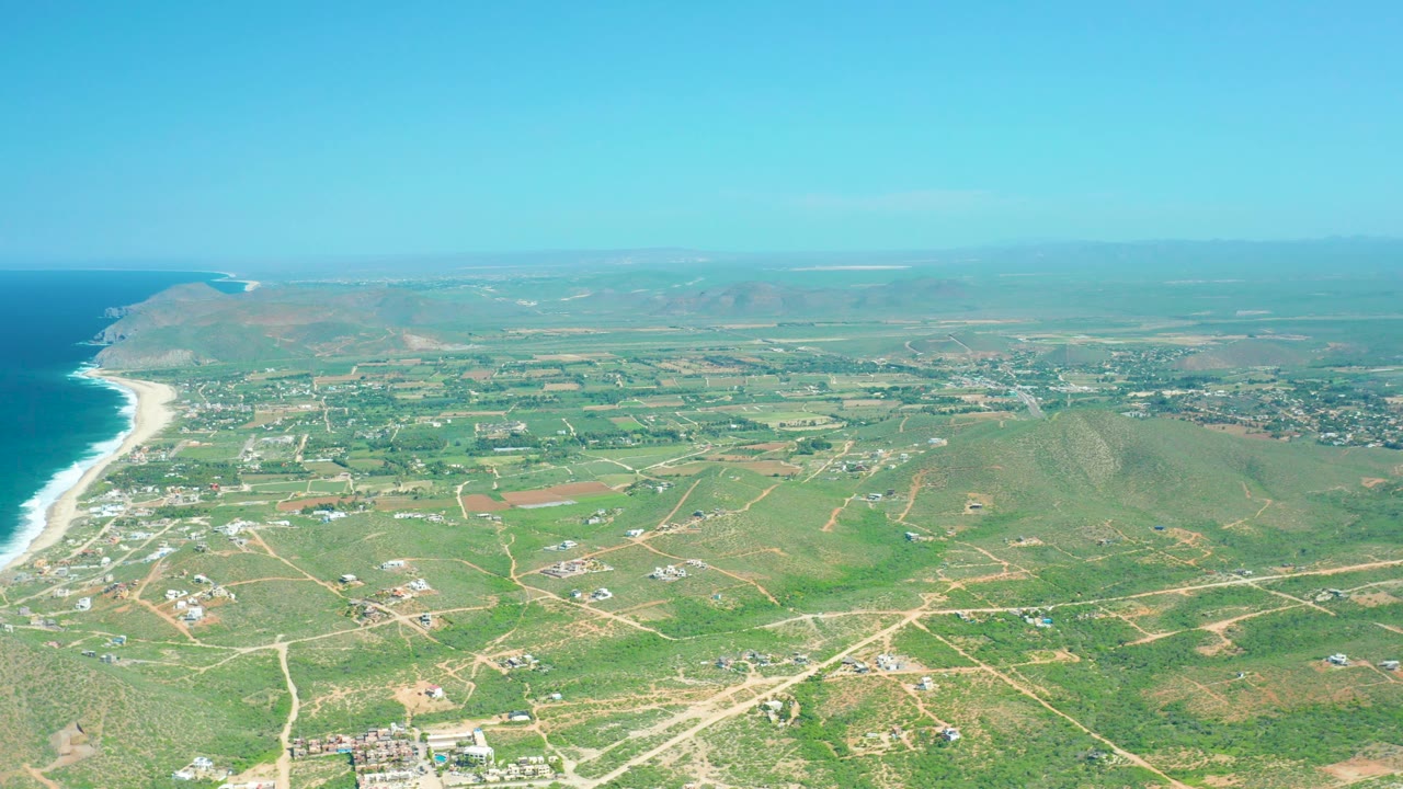 Ocean beach and inland green fields crossed by dirt roads.