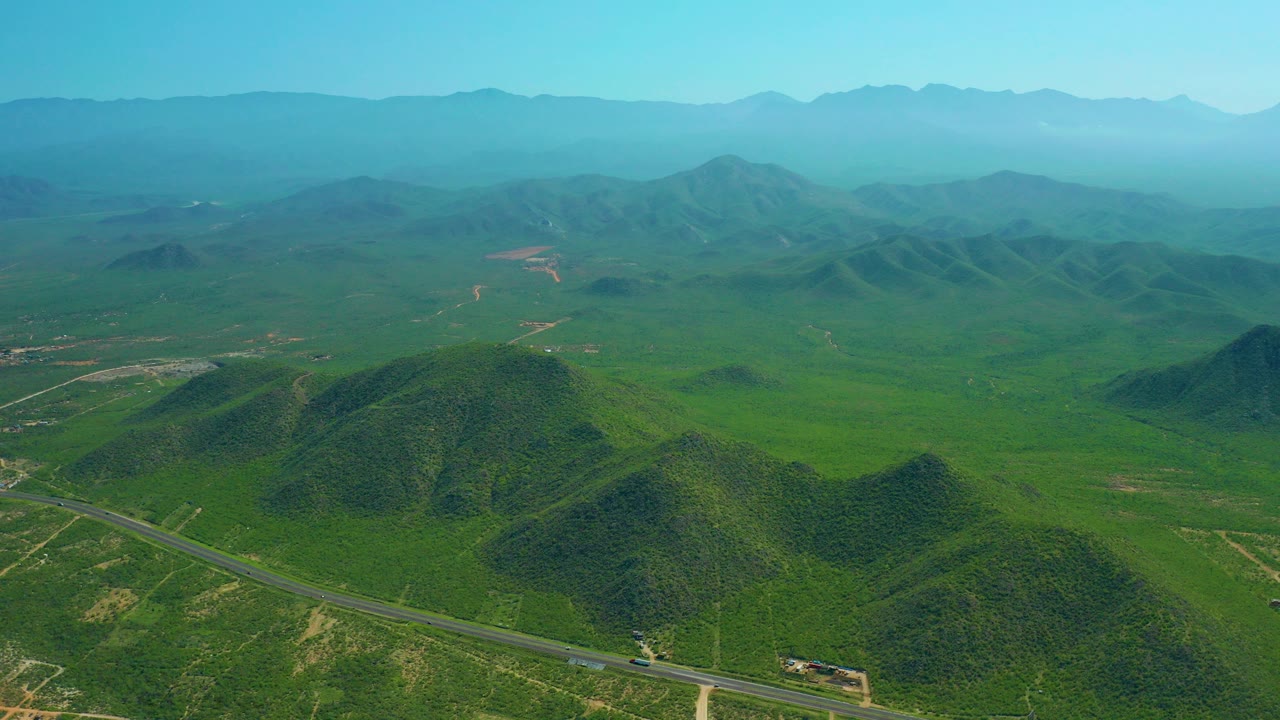 Aerial view of a winding road through green hills with distant mountains.