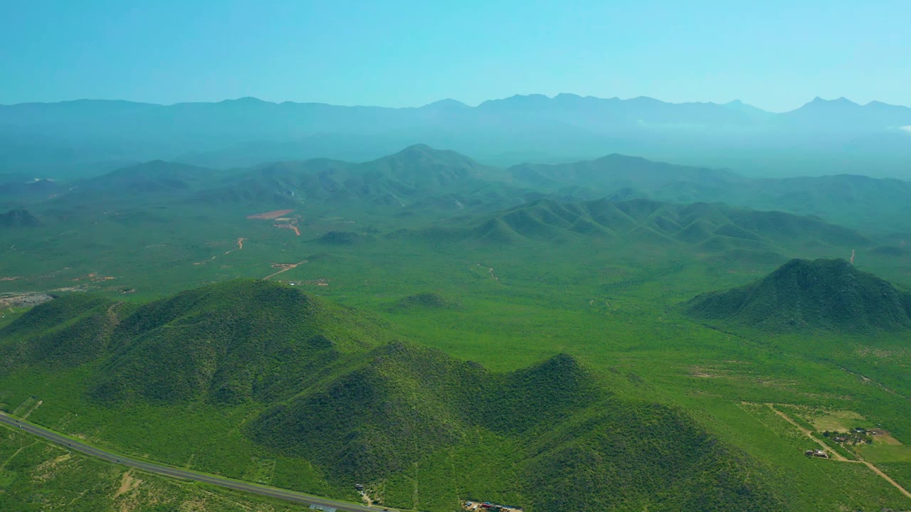 Green valley and rounded hills with a paved road across the lower frame.