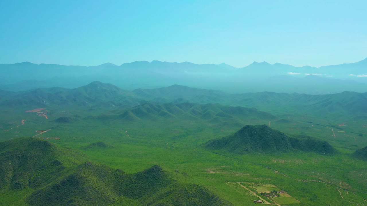 Wide aerial of rolling green hills under a clear blue sky.