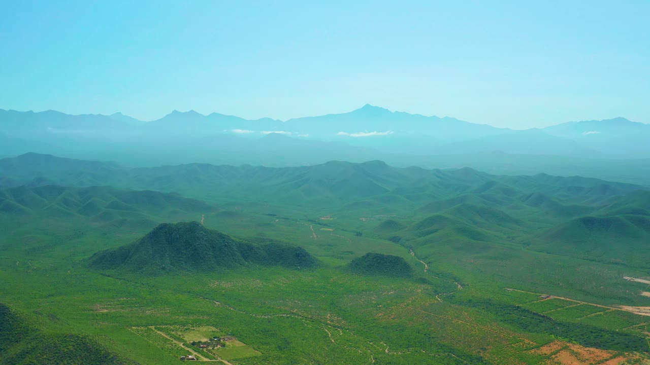 Wide aerial landscape with rounded green hills and mountain horizon