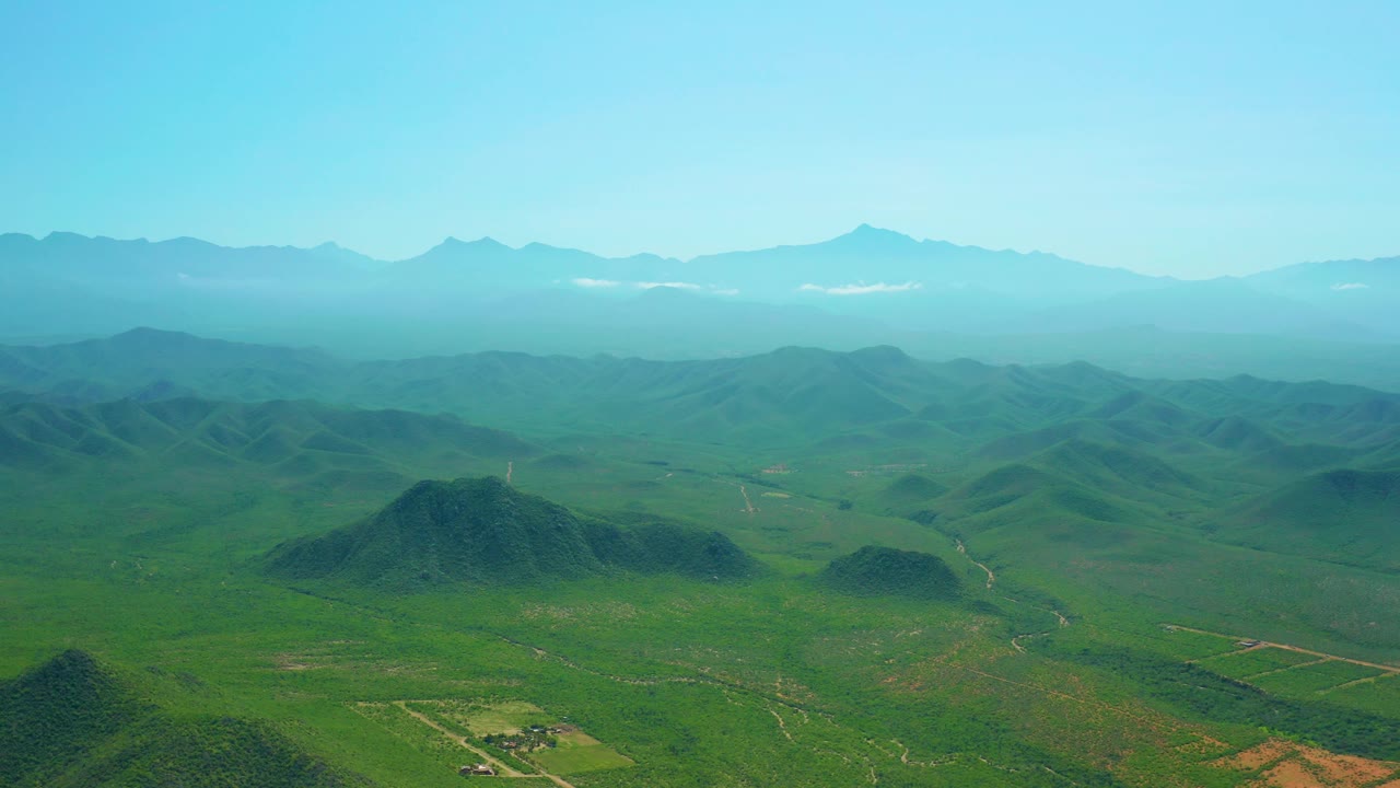 Aerial view over grassy hills with a hazy mountain range beyond