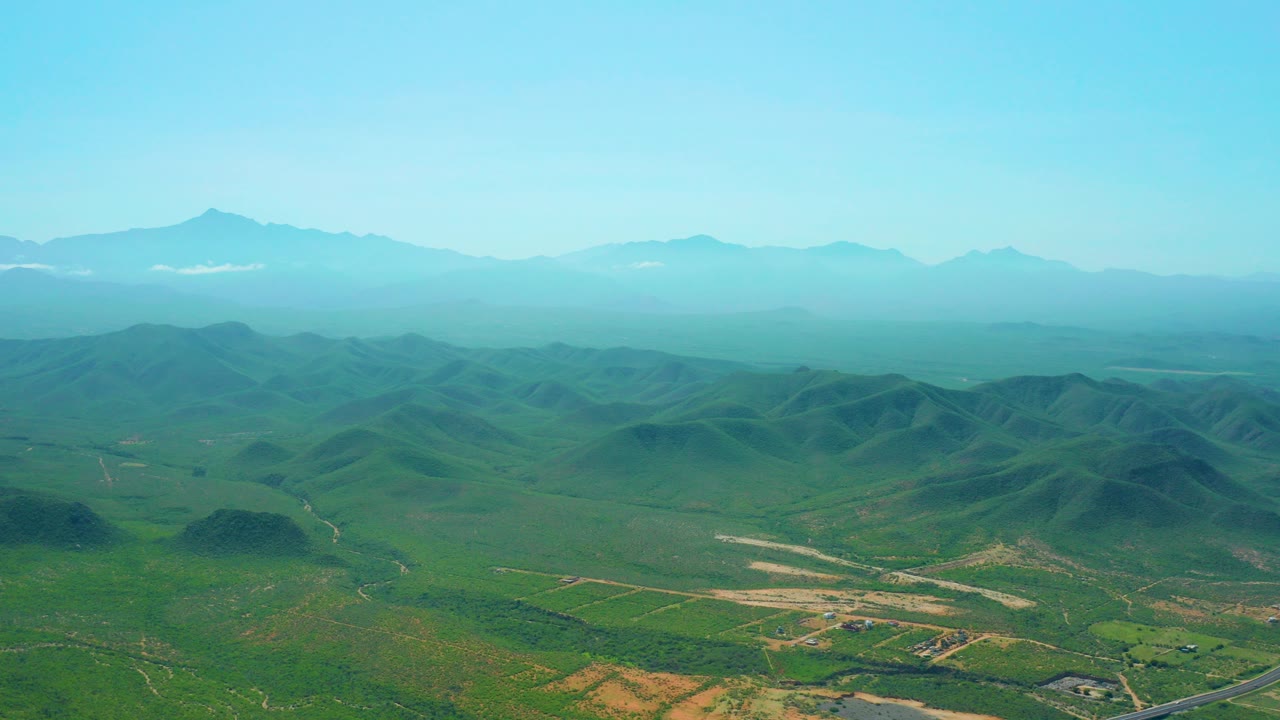 Aerial view of green valley, rolling hills, distant mountains, and clear blue sky.