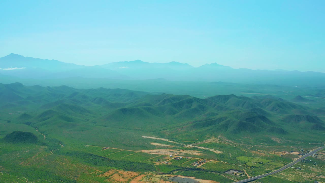 High aerial over green hills and valley with distant blue mountains.