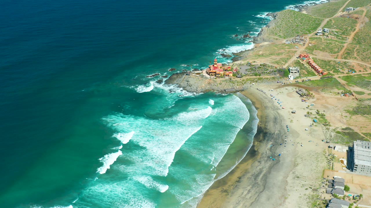 Aerial view of surf curling across turquoise water beside a sandy beach.