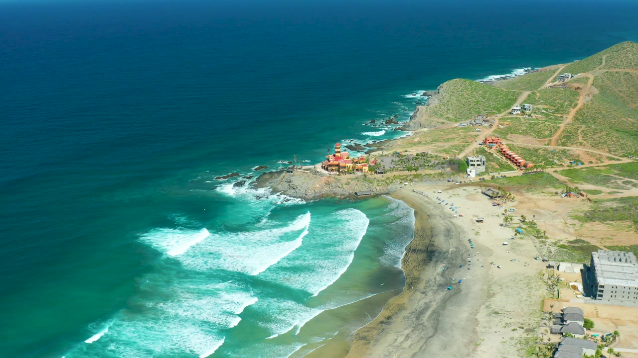 Wide aerial beach scene with waves breaking near a rocky point.