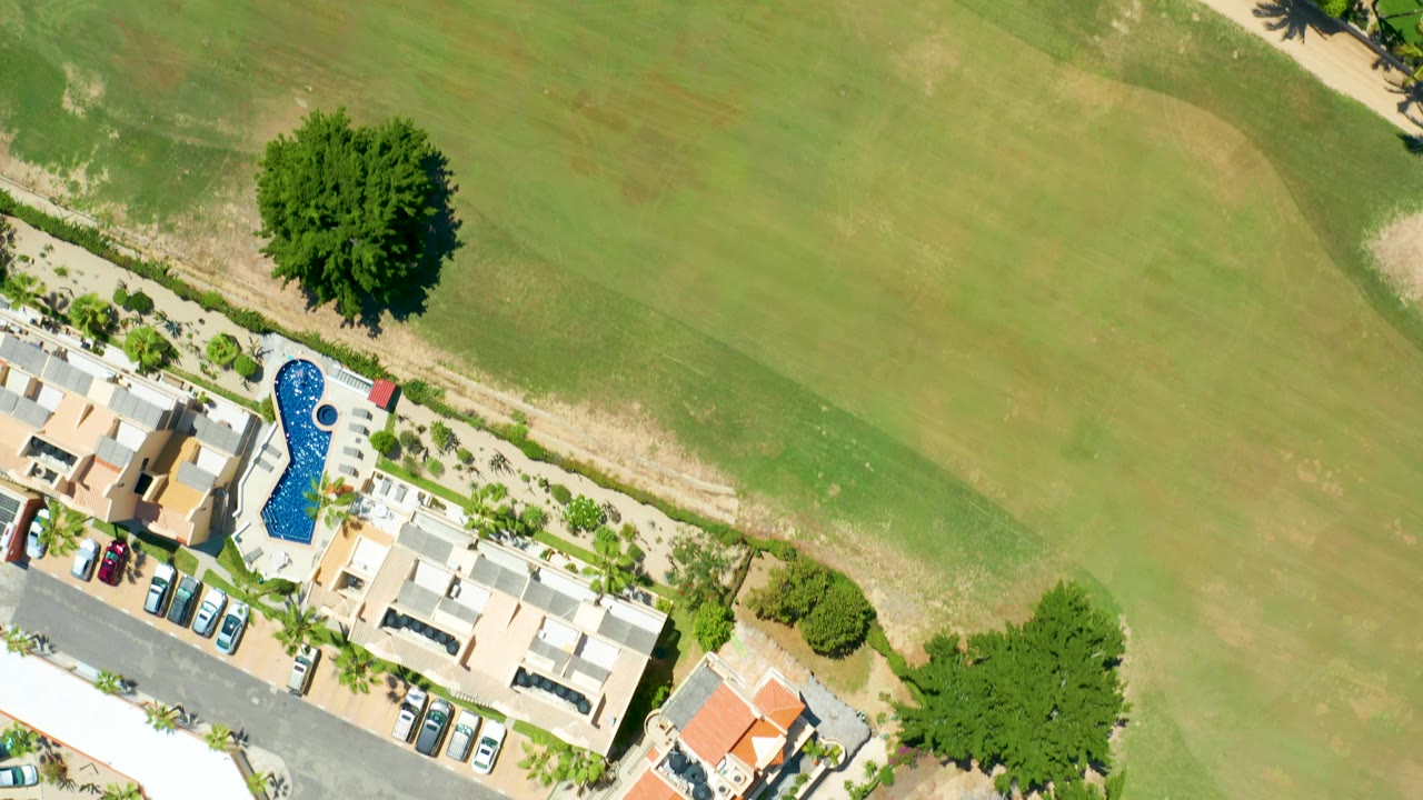 Aerial view with more golf course grass, villas and a blue pool along the lower edge.