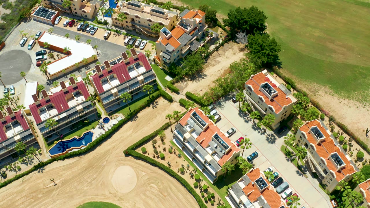 Residential roofs and pool near tan golf-course sand and green fairway.