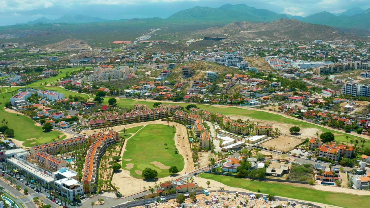 Elevated view of green fairways, red-roof housing, roads, and hillside development.