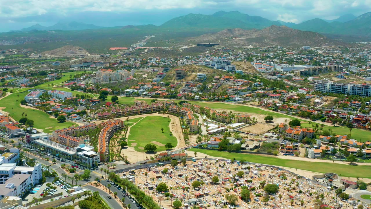 Aerial neighborhood view with green fairways, clustered homes, roads, and mountains.