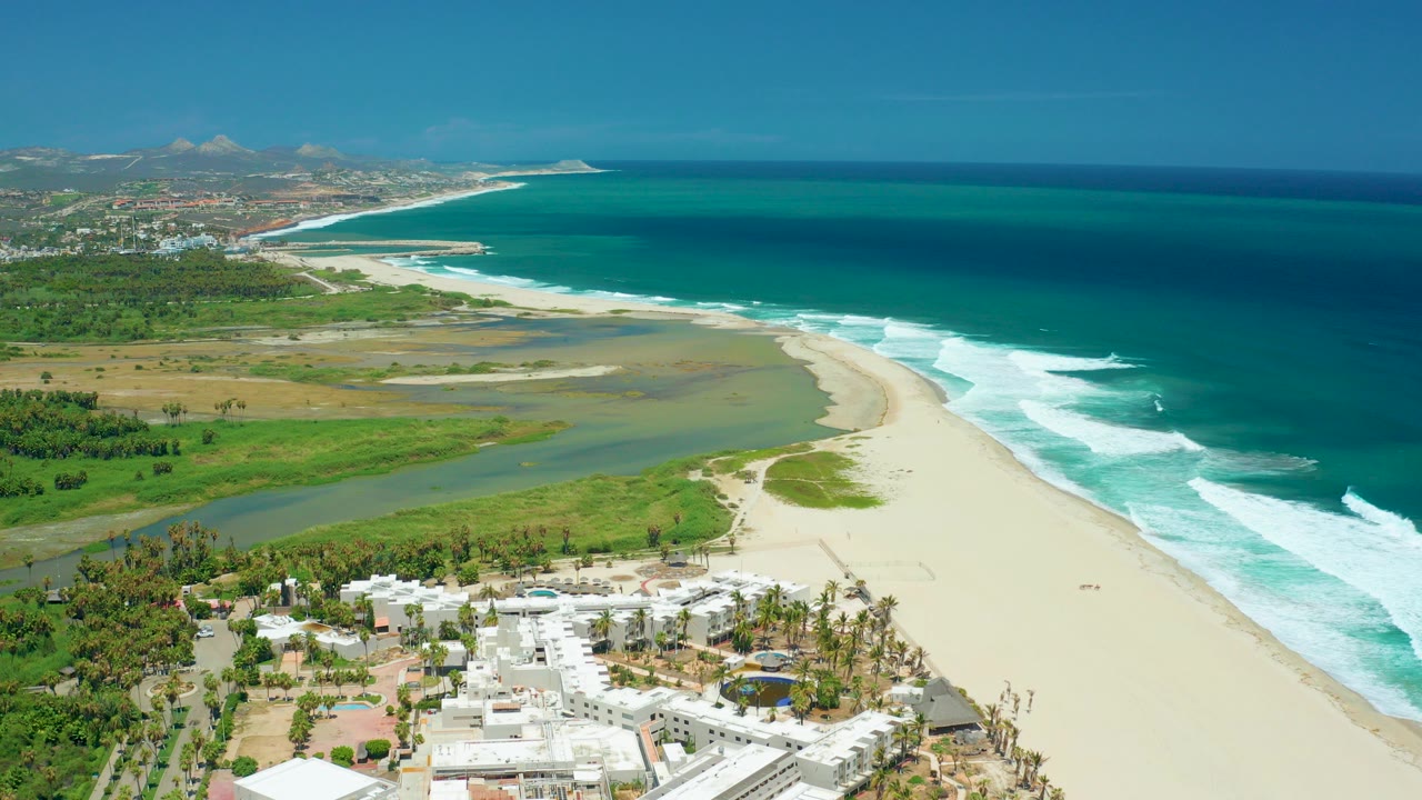 Aerial view of a sandy beach, river lagoon, ocean surf, and coastal buildings.