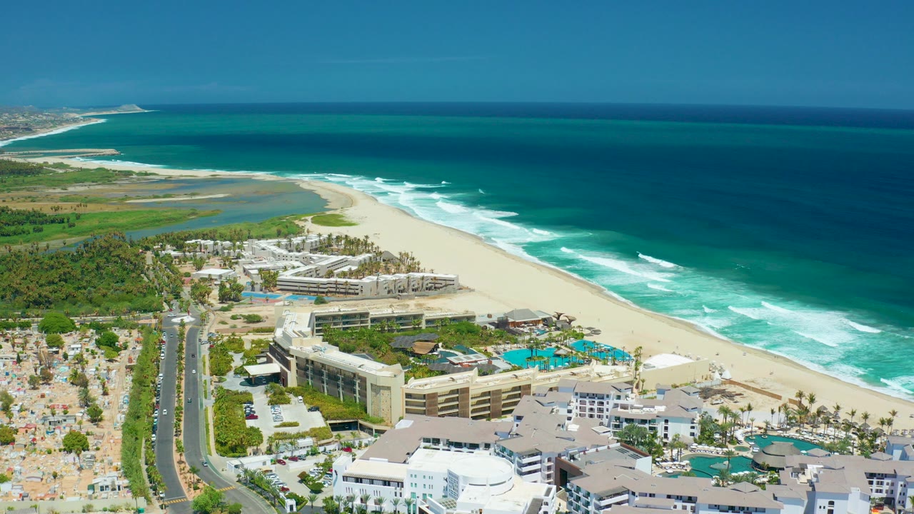 Aerial view of a beachfront resort, pools, road, sand, surf, and ocean.