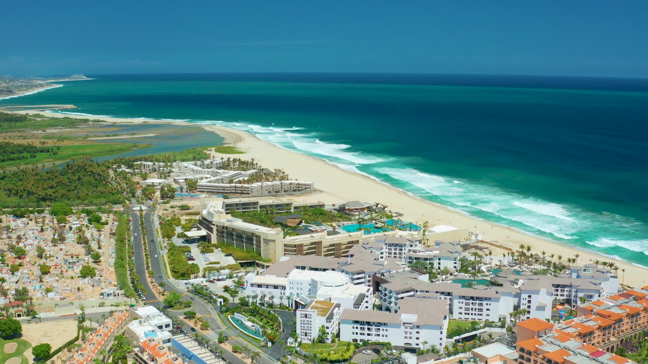 Aerial view of beach resort buildings beside surf and a coastal road.