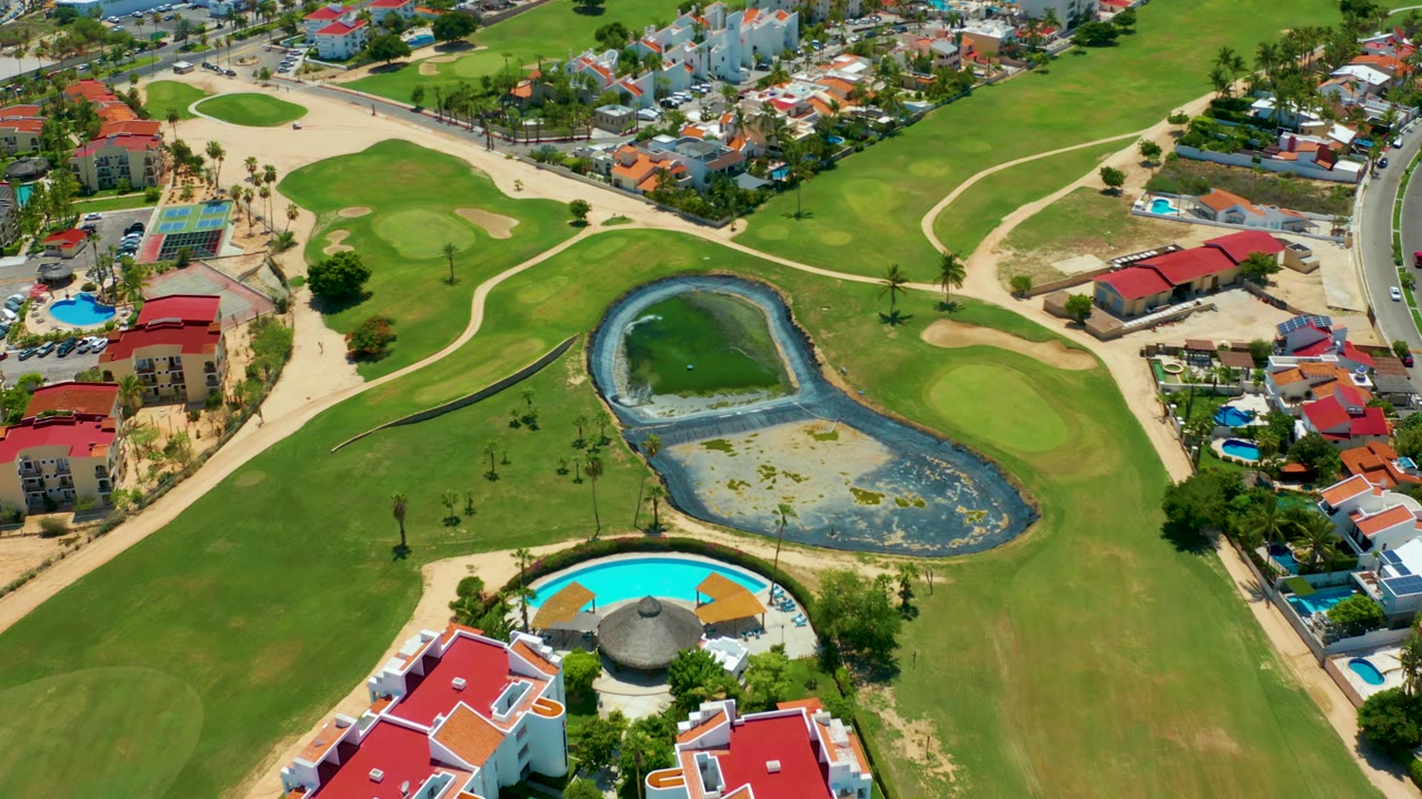 Aerial view of a residential edge beside golf fairways, a pond, and sandy paths.
