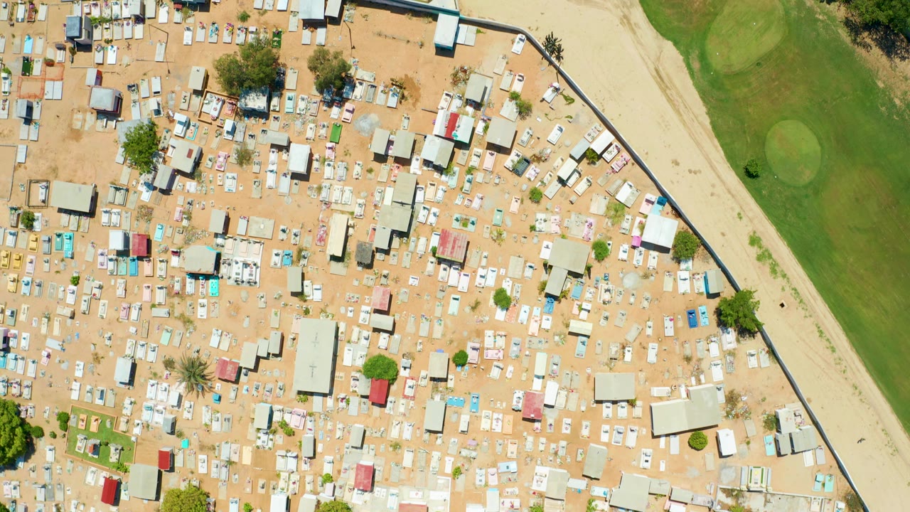 Overhead view of packed rooftops, sandy lots, and a green field to the side.