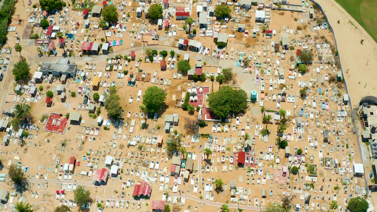 Overhead view of a tent camp with larger trees and clusters of small shelters.