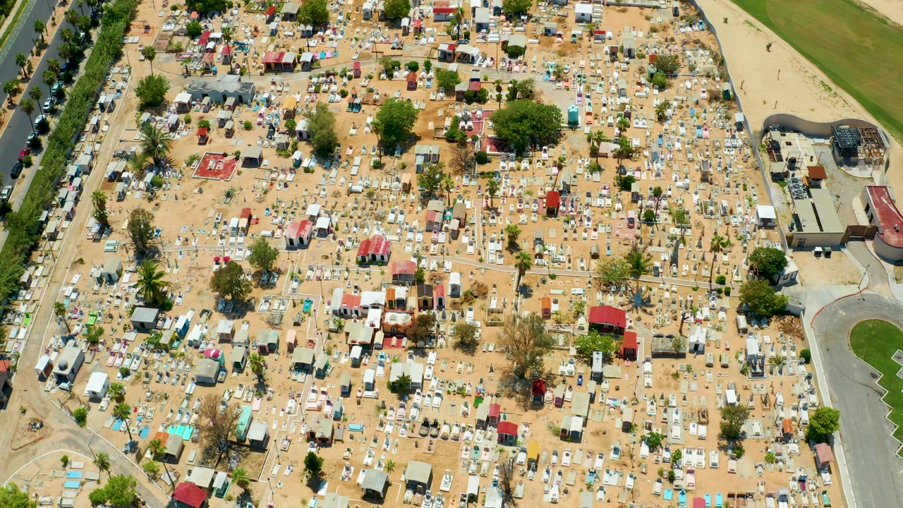 Overhead frame of the San Jose Del Cabo storage area with white and gray RVs, red-roofed structures, trees, a curved paved area on the right, and no visible people.