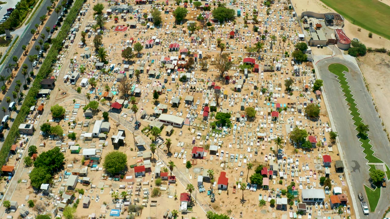 Aerial view across grave markers, trees, and roadside edges.