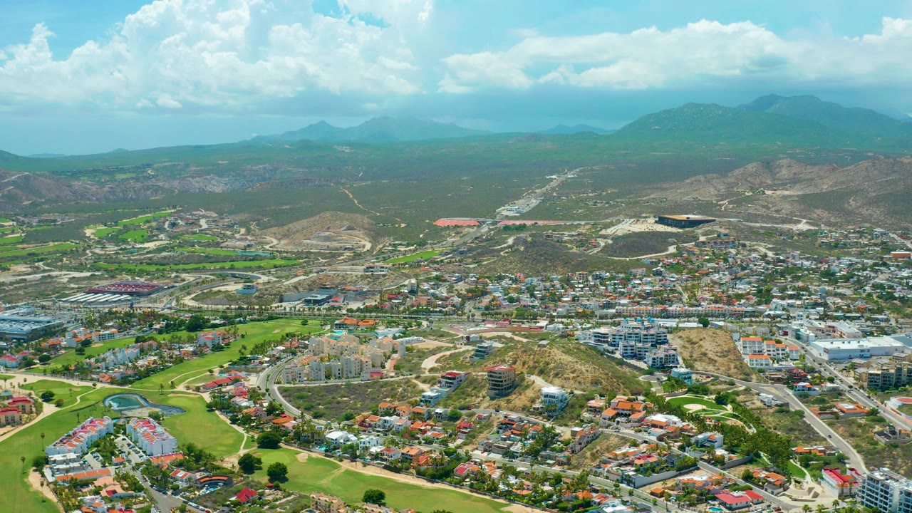 Town and golf course below a cloud-filled sky and mountain backdrop
