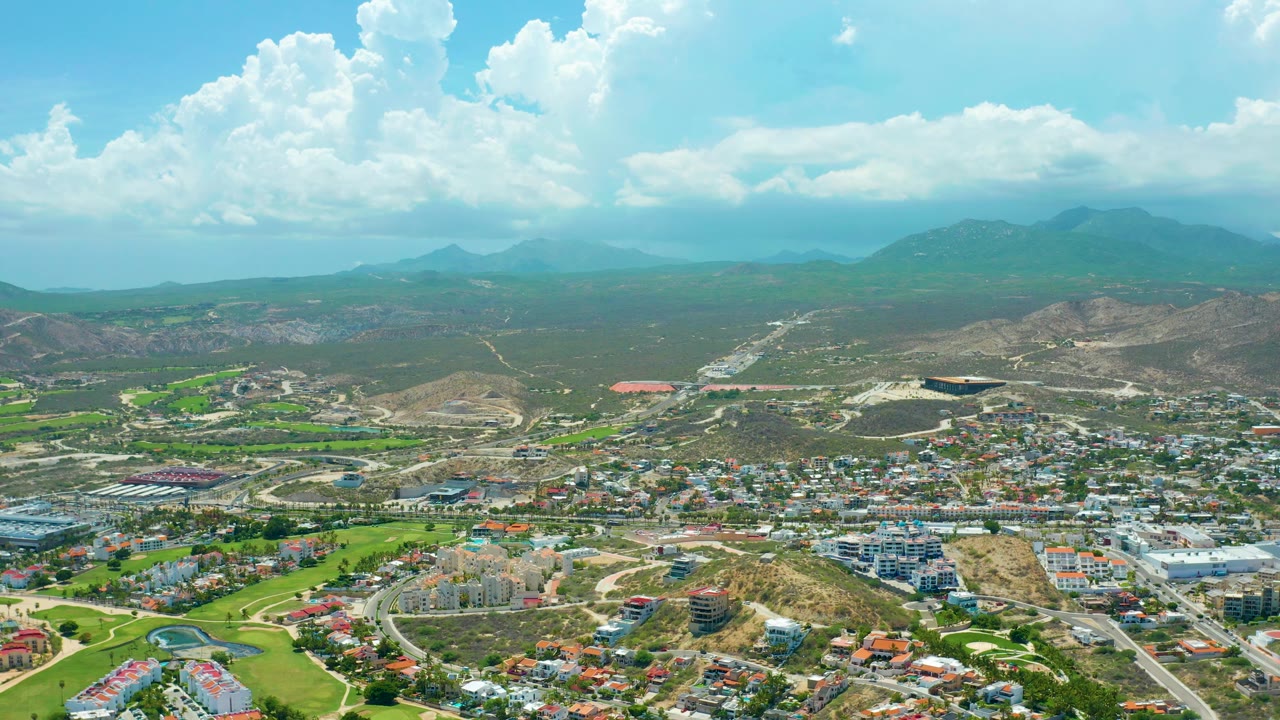 Town and valley landscape with green fields, roads, hills, and cloud shadows.